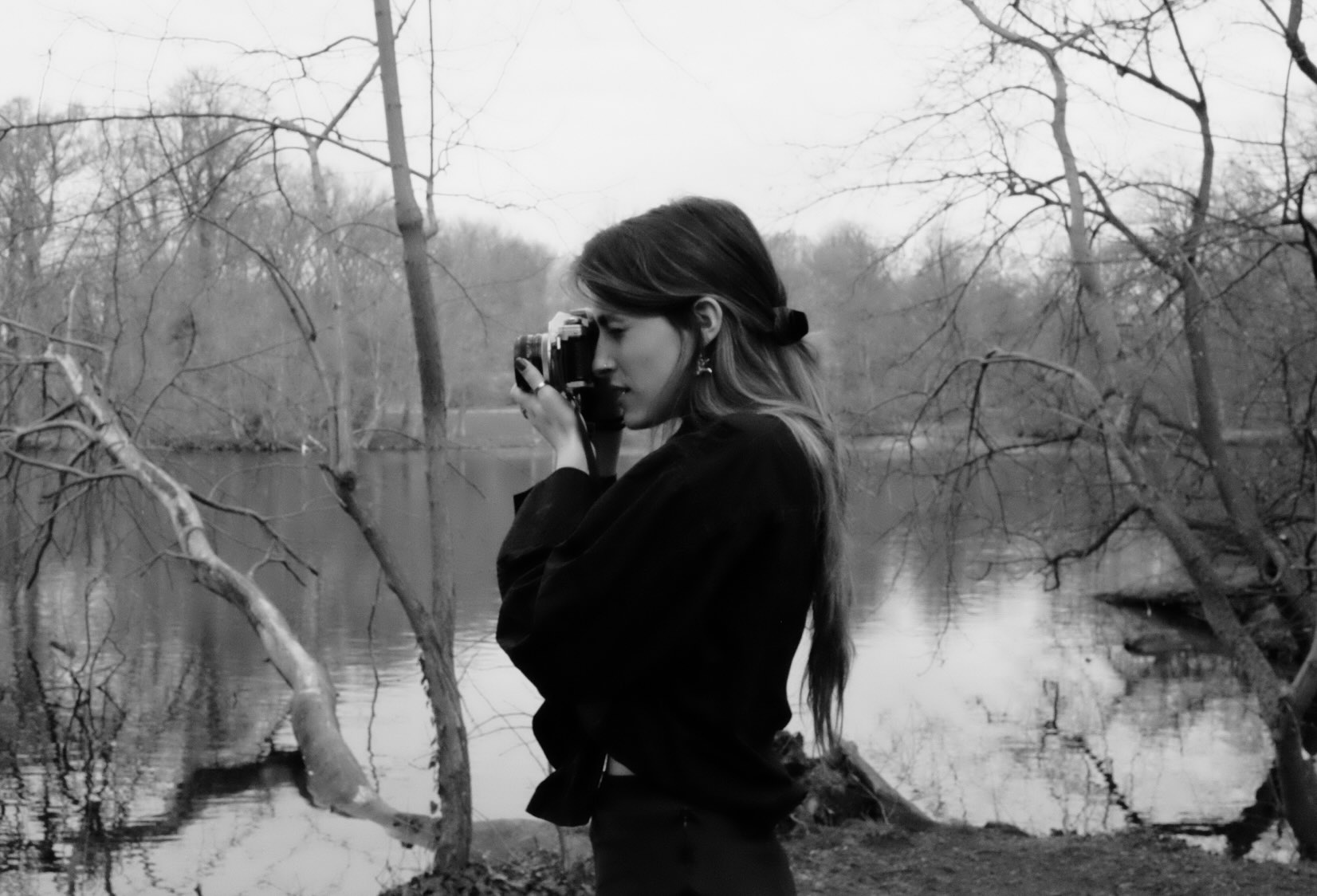 Photograph of student holding camera taking a photograph in front of a lake